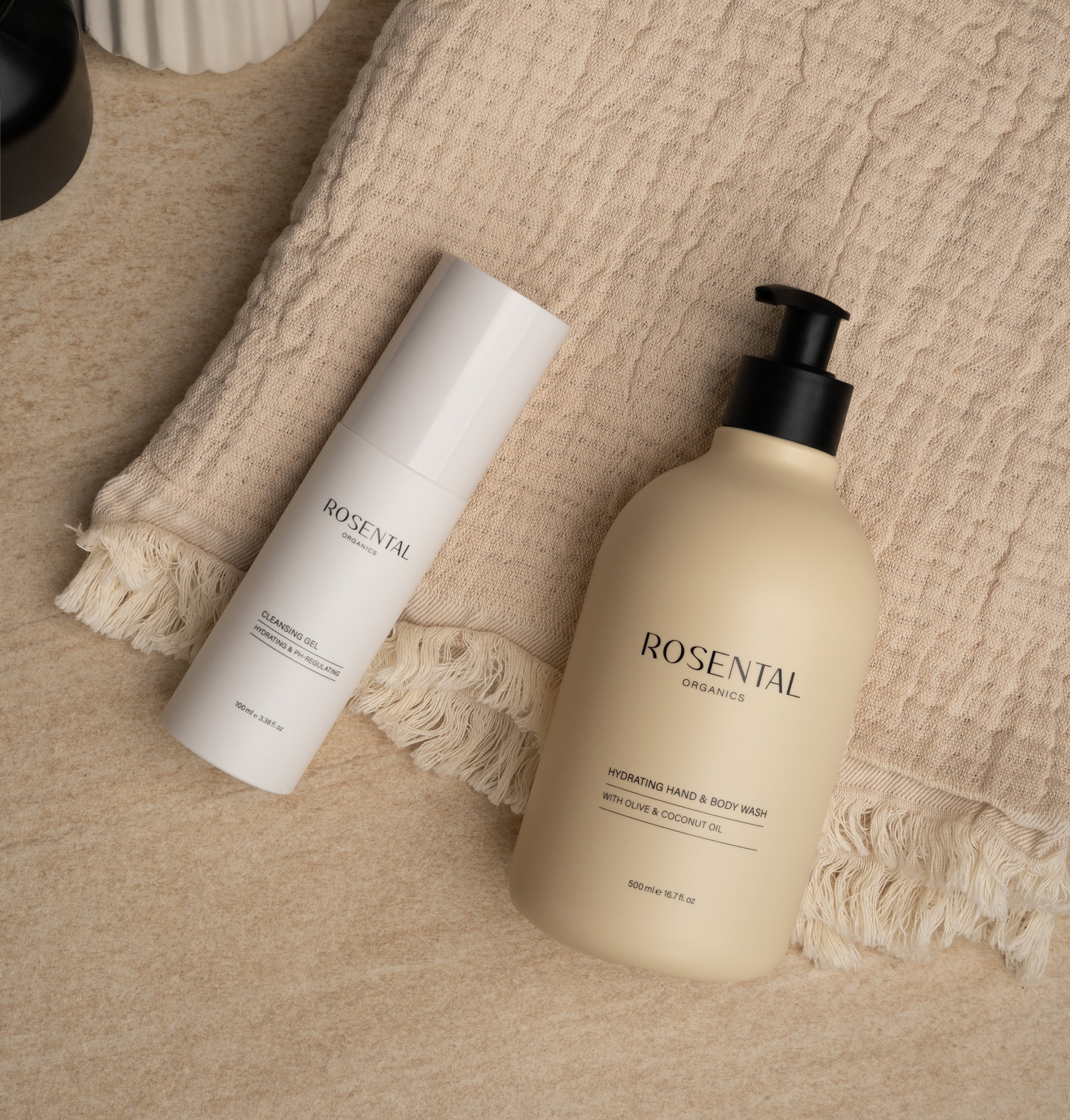 Hydrating Hand & Body Wash in beigefarbenem Pumpspender, liegend auf einem beigen Handtuch auf Marmoroberfläche.