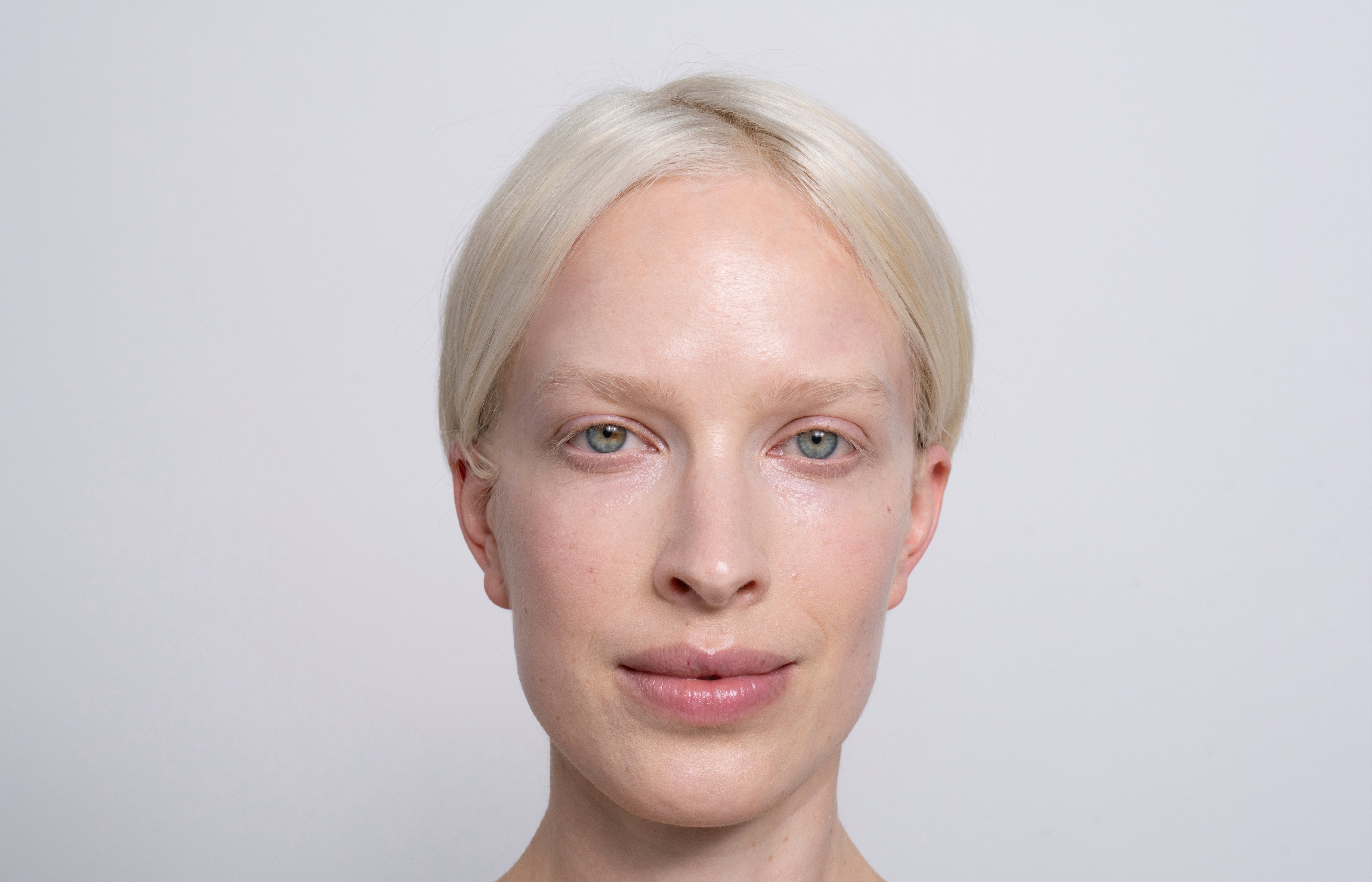 Frau mit weißen Haaren, blauen Augen und ebenmäßiger Haut blickt wach und aufmerksam in die Kamera.